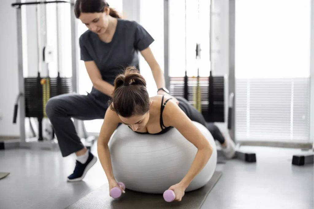 Eien FysioStil Sportphysiotherapeutin die mit einer Patientin auf einem Gymnastikball Sportphysiotherapie-Übungen durchführt.